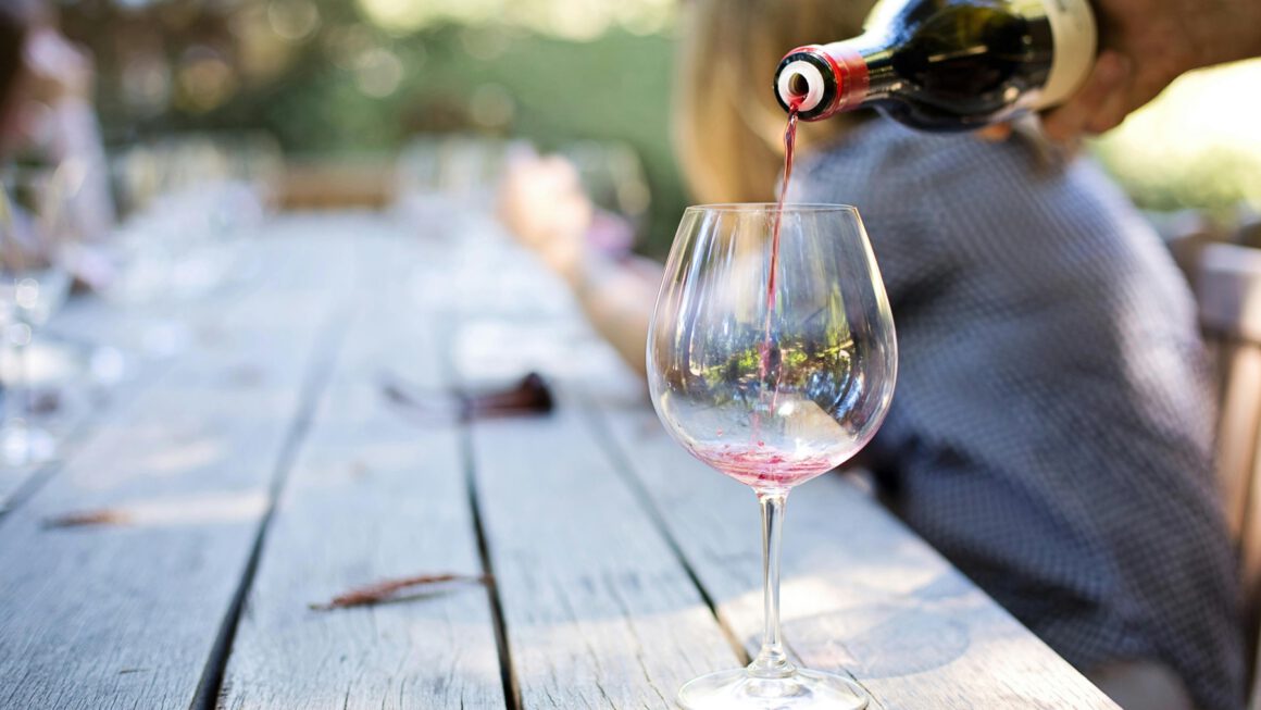 Iemand schenkt een glas rode wijn in